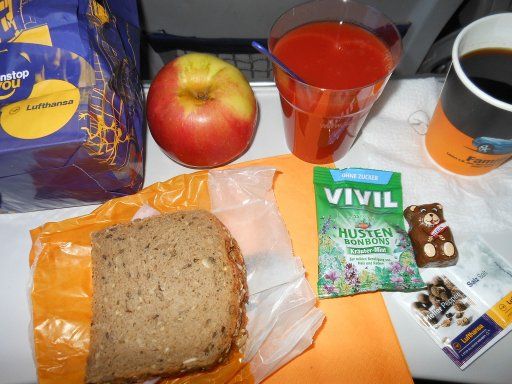 Lufthansa®, Frühstück mit Käse oder Schinkenbrot, Apfel, Schokolade, Husten Bonons, Tomatensaft und Kaffee