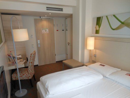 H+ Hotel München (ehemals Treff Hotel München City Centre), Deutschland, Zimmer 407 mit Tisch, Stuhl, Schrank, Minisafe, Kofferablage und Eingang zum Zimmer und Bad