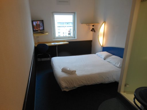 ibis budget Salford Quays, Manchester, Großbritannien, Zimmer 737 mit Doppelbett, Flachbildfernseher, Tisch, Stuhl, Fenster und Kleiderbügel an der Eckgarderobe