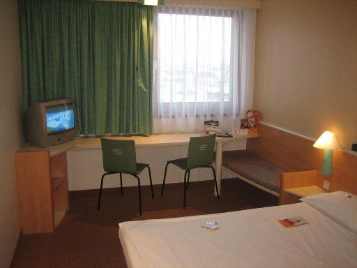 Ibis Wien Mariahilf, Österreich, Zimmer 920, Doppelbett, Sitzbank, Fernseher, Tisch, zwei Stühle und Fenster