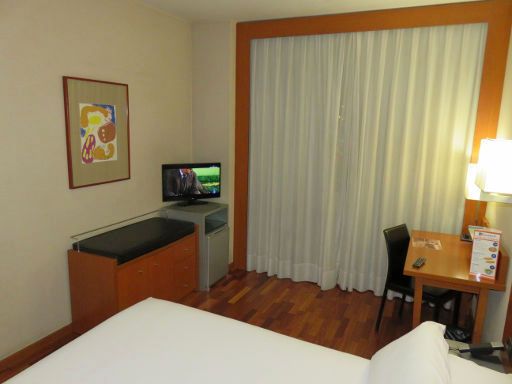 Hotel H2 Granada, Spanien, Zimmer 123 mit Kofferablage, Schrank mit Minisafe, Fernseher, Kühlschrank, Fenster, Stuhl und Schreibtisch