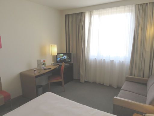 Novotel Valladolid, Spanien, Zimmer 412 mit Kofferablage, Schreibtisch, Stuhl, Fernseher, Fenster, Vorhängen und Sofa